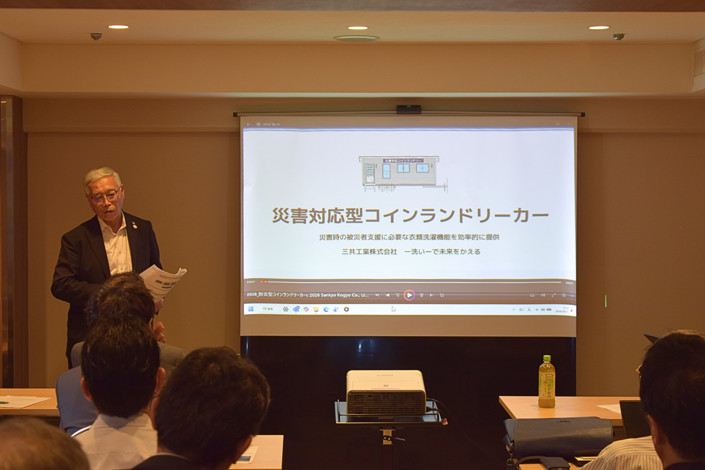 災害対応型コインランドリーカーの資料を示しながら説明する日コ連の宮澤敏文理事長